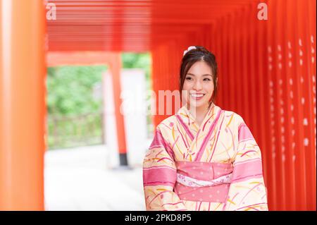 Une femme dans un yukata marche à travers la porte torii d'un sanctuaire Banque D'Images