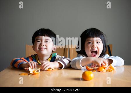 Les enfants rient en épluchant des mandarines Banque D'Images