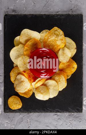 Vue de dessus de tas de pommes de terre frites avec sauce à trempette rouge sur le plateau de service en ardoise noire sur la table en plâtre gris. Présentoir de snacks haut de gamme Banque D'Images