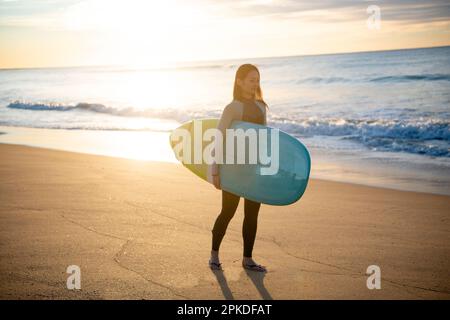 Femme marchant sur la plage avec une planche de surf Banque D'Images