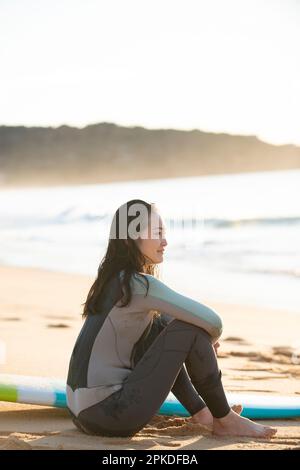 Femme en combinaison assise sur une plage de sable Banque D'Images