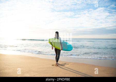 Femme marchant sur la plage tenant une planche de surf Banque D'Images