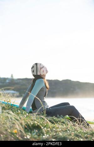 Femme en combinaison assise sur la plage en riant Banque D'Images