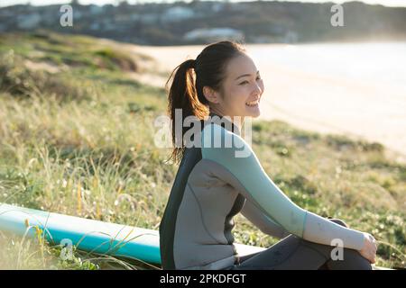 Femme en combinaison assise sur la plage en riant Banque D'Images