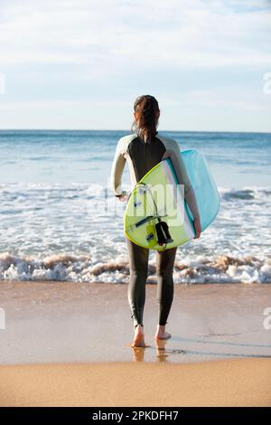 Femme marchant sur la plage avec une planche de surf Banque D'Images