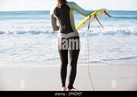 Femme en combinaison transportant une planche de surf dans l'eau Banque D'Images