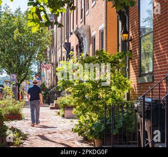 Un homme portant une casquette de baseball descend une rue remplie de charmantes maisons en rangée de briques à Harrisburg, en Pennsylvanie Banque D'Images