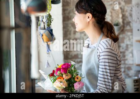 Femme souriante d'un magasin tenant un bouquet de fleurs et regardant dehors Banque D'Images