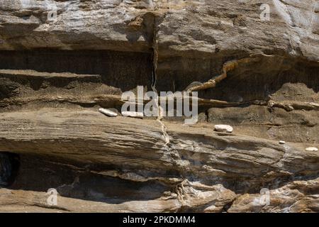 Roche structurée sur un côté de la plage. Diverses textures du matériau rugueux et des petits cailloux. Plage de Livadi, île de Thassos (Tassos), Grèce. Banque D'Images