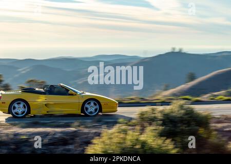 Une voiture de sport jaune voyageant le long d'une route sinueuse avec des montagnes majestueuses en arrière-plan. Banque D'Images
