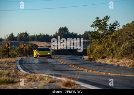 Une voiture de sport jaune voyageant le long d'une route sinueuse avec des montagnes majestueuses en arrière-plan. Banque D'Images