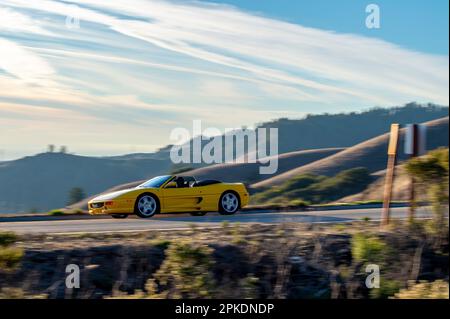 Une voiture de sport jaune voyageant le long d'une route sinueuse avec des montagnes majestueuses en arrière-plan. Banque D'Images