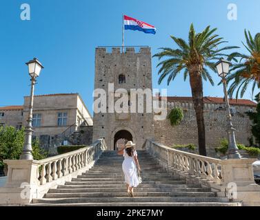 Jeune femme en robe blanche marchant sur les escaliers menant à la tour et à la porte principale de la ville à Korcula, Croatie Banque D'Images