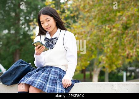 Une étudiante en uniforme scolaire regardant son téléphone Banque D'Images