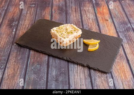 Une tranche de tarte au citron avec un biscuit sur un plateau en ardoise noire Banque D'Images