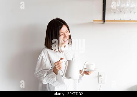 Femme riant avec une bouilloire électrique et une tasse Banque D'Images