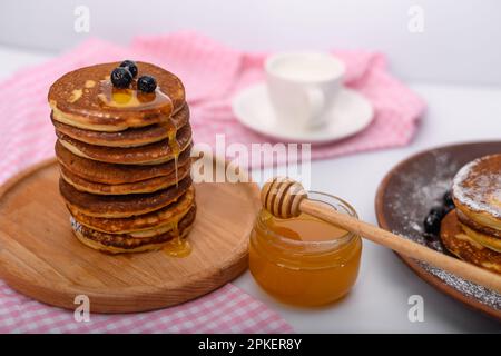 une pile de crêpes sur un plateau en bois et un pot de miel. Banque D'Images