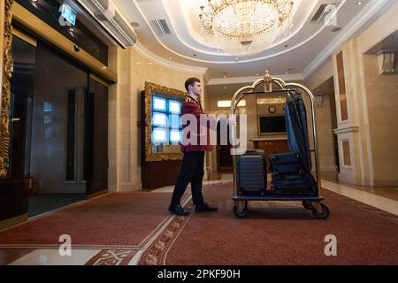 Le groom en uniforme traditionnel transporte une voiturette avec des bagages le long du hall Banque D'Images