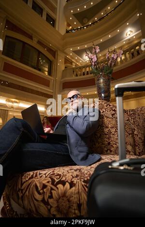 Imposant homme assis avec un ordinateur portable sur un canapé en velours Banque D'Images