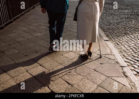 Vieux couple à pied dans la vieille ville. Femme en train de faire des limonces avec la canne et homme marchant dans la rue, vue arrière. Banque D'Images