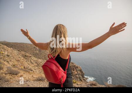Une femme à bras ouverts observe la mer, concept de l'insouciance et de la tranquillité d'esprit. Banque D'Images