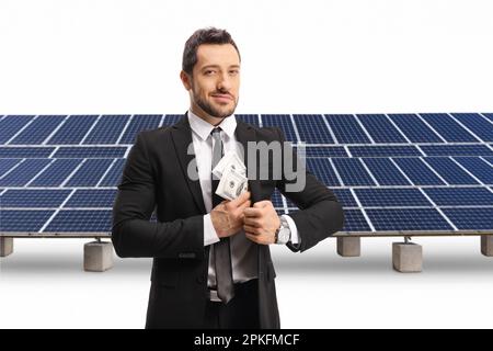 Homme d'affaires mettant de l'argent dans sa poche et se tenant devant des panneaux solaires isolés sur fond blanc Banque D'Images