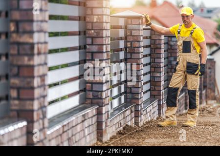 Briques en béton et panneaux en aluminium fabriqués à partir de clôture résidentielle. Travailleur de la construction caucasien dans son 40s. Banque D'Images