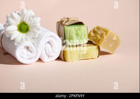 Serviette blanche, fleur de camomille et pile de barres de savon bio avec des ingrédients naturels, isolée sur beige. Concept spa Banque D'Images