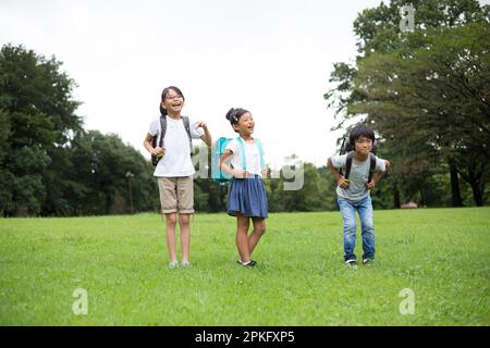 Les enfants des écoles primaires se tenant sur un terrain herbeux dans un parc avec leurs sacs à dos d'école Banque D'Images