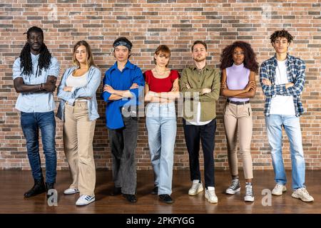 Groupe de jeunes posant devant un mur de briques, expressions sérieuses et décisives Banque D'Images