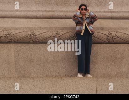 Une jeune femme d'Asie de l'est debout seule sur la plinthe entourant la colonne de Nelson à Trafalgar Square, Londres, Angleterre. ROYAUME-UNI Banque D'Images