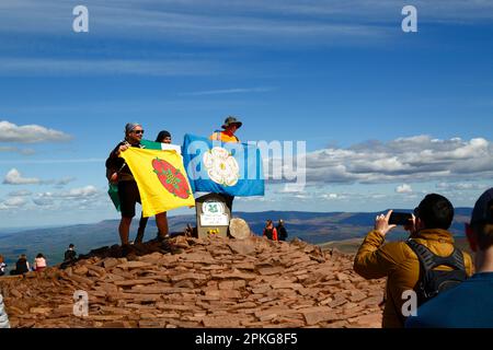 Météo au Royaume-Uni : jour férié du Vendredi Saint, 7 avril 2023. Parc national de Brecon Beacons, pays de Galles du Sud. Les randonneurs portant les drapeaux du Lancashire et du Yorkshire ont pris leur photo sur le point de trig sur le sommet de Pen y Fan dans le parc national de Brecon Beacons. Pen y Fan (886m / 2 907ft) est le plus haut sommet du parc national de Brecon Beacons et de la Grande-Bretagne du Sud et une destination populaire de randonnée. Par beau temps ensoleillé, beaucoup de gens ont fait le voyage au parc pour les vacances d'aujourd'hui. Banque D'Images