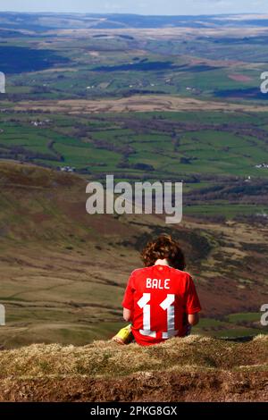 Météo au Royaume-Uni : jour férié du Vendredi Saint, 7 avril 2023. Parc national de Brecon Beacons, pays de Galles du Sud. Un garçon portant un maillot de football Gareth Bale #11 Wales joue avec son smartphone au sommet de Pen y Fan dans le parc national de Brecon Beacons. Par beau temps ensoleillé, beaucoup de gens ont fait le voyage au parc pour les vacances d'aujourd'hui. Banque D'Images