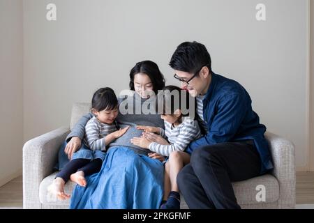 Petite sœur et père mettant leurs mains sur le ventre de la mère enceinte Banque D'Images