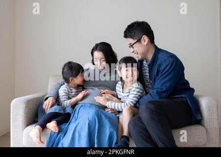 Petite sœur et père mettant leurs mains sur le ventre de leur mère enceinte Banque D'Images