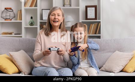 Grand-mère émotive dans ses 60s et petite-fille de jouer des jeux vidéo sur les gamepads, ayant le plaisir. La grand-mère de femme senior gagne le jeu et Banque D'Images