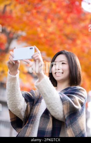 Femme prenant une photo des feuilles d'automne avec un smartphone Banque D'Images
