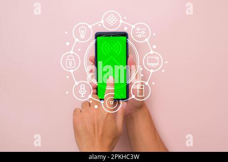 Main d'homme tenant le smartphone sur fond rose avec interface de technologie Smart Home sur l'écran de l'application pour smartphone. Concept d'automatisation. Banque D'Images