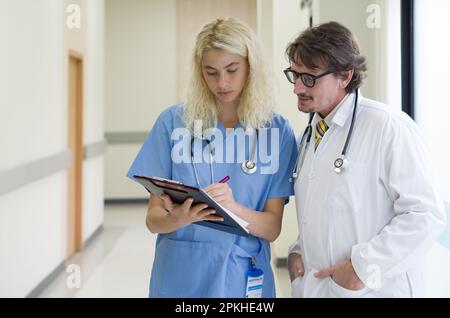 Médecin caucasien principal ayant discuté dans un couloir d'hôpital avec une infirmière. Équipe de médecins travaillant ensemble sur le dossier des patients à l'hôpital. Médecin Banque D'Images