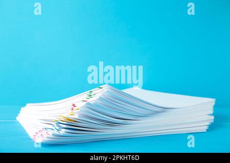 Trombone coloré avec pile de papier blanc sur bleu. Vue de dessus Banque D'Images
