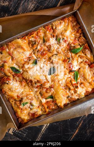 Gros plan d'une lasagne italienne traditionnelle à base de sauce bolognaise au bœuf haché et de feuilles de basilic servies sur une table rustique en bois sombre Banque D'Images