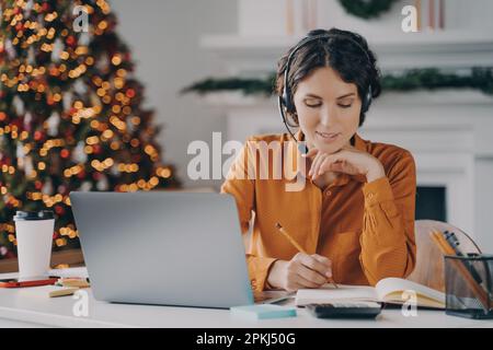 Micro-casque/oreillette avec micro, paradateur européen pour centre d'appels féminin, prenant des notes à l'ordre du jour tout en parlant avec le client via un ordinateur portable en ligne, fonctionne à domicile avec XMA Banque D'Images