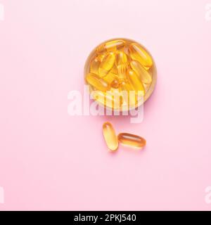 Capsules transparentes jaunes d'huile de poisson sur fond rose. Vitamines, compléments alimentaires. Banque D'Images