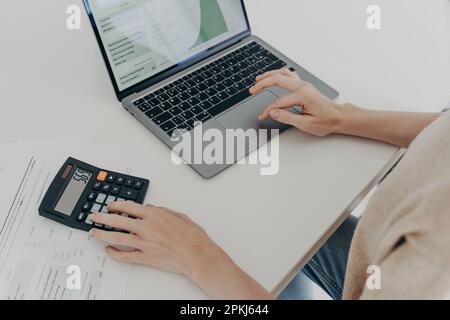 Plan court d'une femme méconnaissable assis au bureau avec ordinateur portable calculatrice et papiers calcule montilement dépenses études de factures d'utilité compte i Banque D'Images