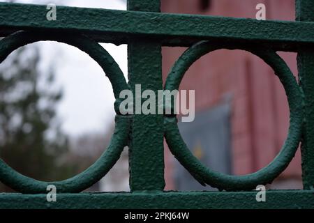 Une vieille clôture en métal forgé avec des pikes, des épingles, des anneaux de l'époque soviétique peints avec de la peinture verte. Banque D'Images