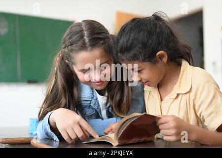Des élèves joyeux lisant le livre sur le bureau dans la salle de classe à l'école Banque D'Images