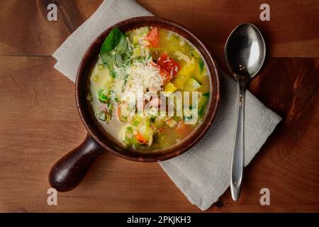 Soupe de légumes italienne minestrone aux haricots et aux pâtes dans un bol rustique en terre cuite avec cuillère et serviette de table Banque D'Images