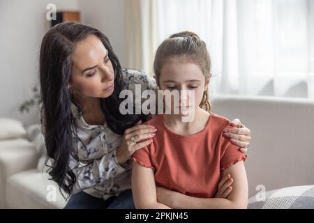 Mère confort bouleverser la fille qui s'assoit avec les bras croisés sur un canapé. Banque D'Images