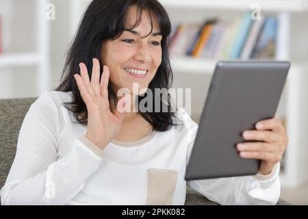femme moderne d'âge moyen assise sur un canapé à la maison à l'aide d'une tablette Banque D'Images