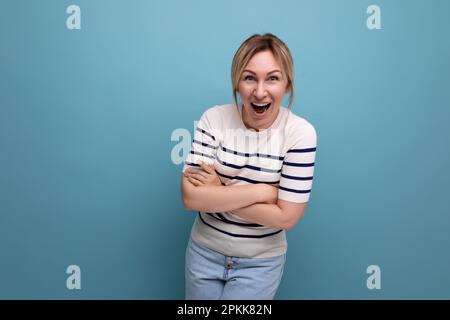 photo horizontale de la femme blonde lumineuse heureuse dans une tenue décontractée riant avec enthousiasme sur fond bleu avec espace copie Banque D'Images